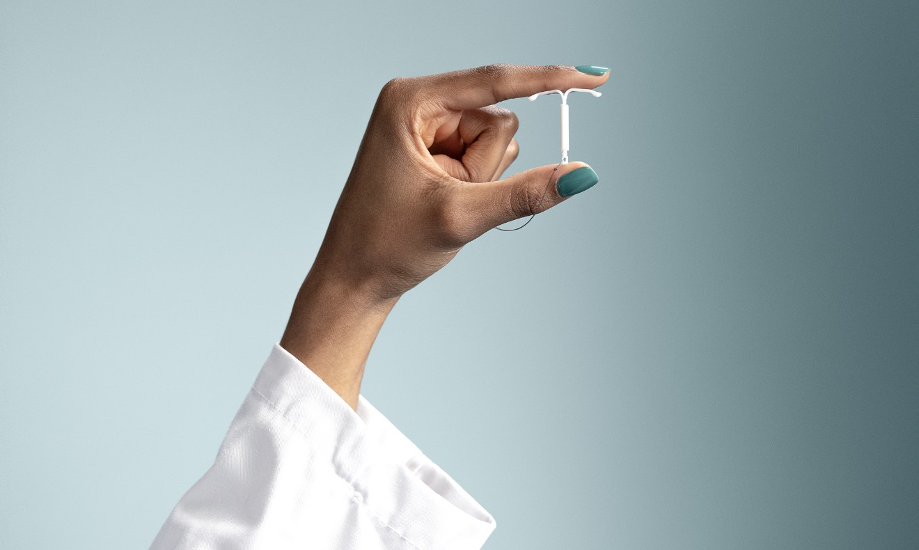 A hand holding a Mirena (levonorgestrel-releasing intrauterine system) 52mg IUD between thumb and index fingers